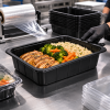 PP 1/2 gastro thermo schaal zwart 325 x 265 x 100 mm in gebruik voor maaltijdverpakking in een professionele keuken, gevuld met pasta, kip en groenten en afgedekt met folie.