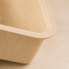 Close-up van een beige bagasse voedseltray waarbij de afgeronde hoek en fijne vezelstructuur van het materiaal scherp in beeld zijn gebracht. De natuurlijke textuur en stevige afwerking worden benadrukt tegen een zachte, neutrale achtergrond met subtiele 