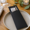 Zwarte papieren bestekhoes met wit servet, vork en mes stijlvol gepresenteerd op een gedekte eettafel met een keramisch bord, ideaal voor restaurants, catering en feestelijke tafelaankleding.