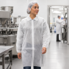 Medewerker draagt een witte PP bezoekersjas van non-woven materiaal in een hygiënische productieomgeving.