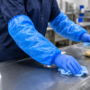 Blauwe DPE mouwovertrekken 20 my 400 mm in gebruik tijdens reinigingswerkzaamheden, voor hygiënische bescherming van de armen in professionele werkomgevingen.
