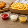 Transparante PP sausbakjes van 30 ml gevuld met ketchup, mayonaise en mosterd, gepresenteerd naast een portie friet en snacks. De afbeelding toont het gebruik van de sauscups voor het serveren van individuele sausporties in horeca, catering en afhaaltoepa