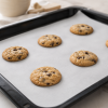 Wit gesiliconeerd bakpapier in gebruik op een zwarte bakplaat met versgebakken chocoladekoekjes, waarbij de anti-aanbakwerking en praktische toepassing van het bakpapier tijdens het bakken duidelijk zichtbaar zijn.