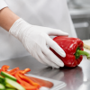 Hand met witte nitril handschoen houdt een rode paprika vast tijdens voedselbereiding.