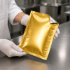 Medewerker controleert een vacuümverpakte zak met gouden voorkant en zilveren achterkant.