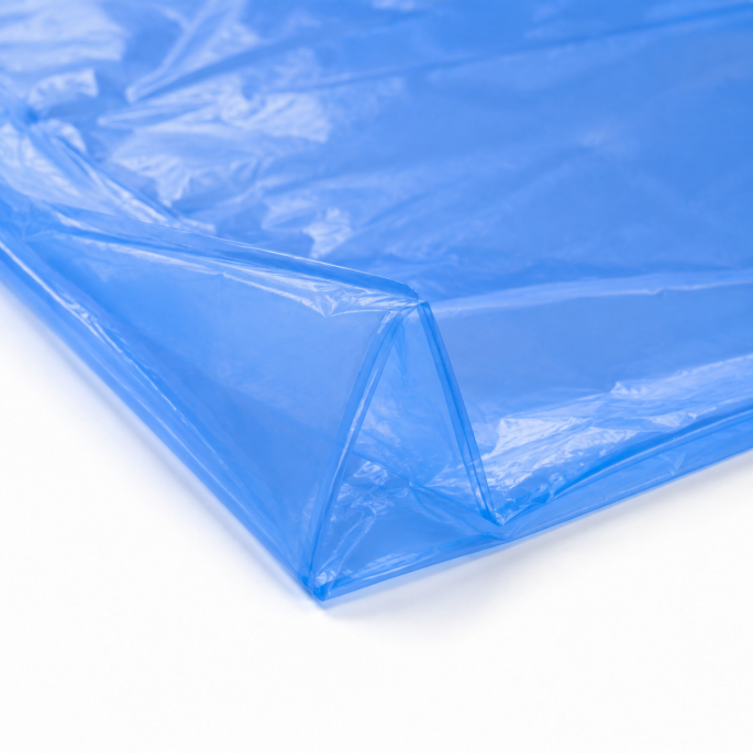 Ingezoomde detailfoto van een lege blauwe HDPE-kratzak van 10 micron, waarbij de dunne transparante folie, zijvouw en afgesloten lasnaad duidelijk zichtbaar zijn tegen een witte achtergrond