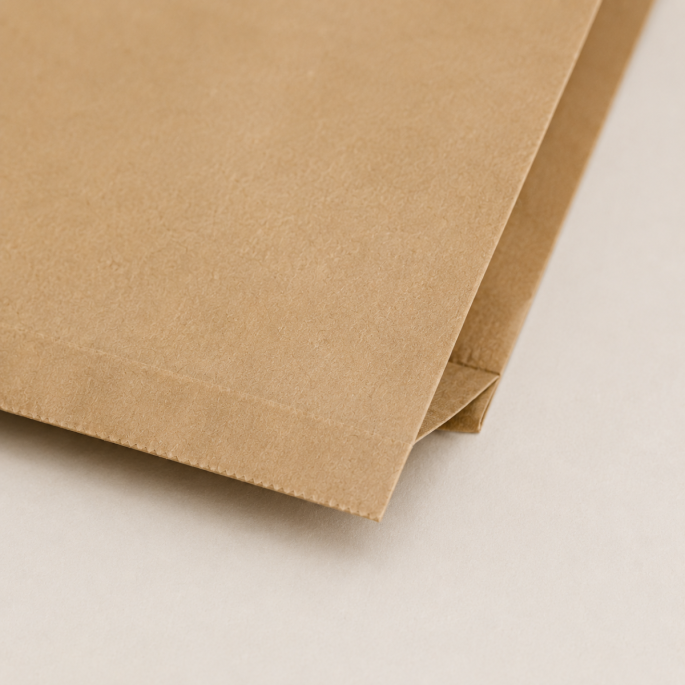 Detailopname van de hoek van een bruin papieren hamburgerzakje van kraftpapier. De close-up laat de stevige vouwconstructie, nette afwerking en natuurlijke papierstructuur zien.