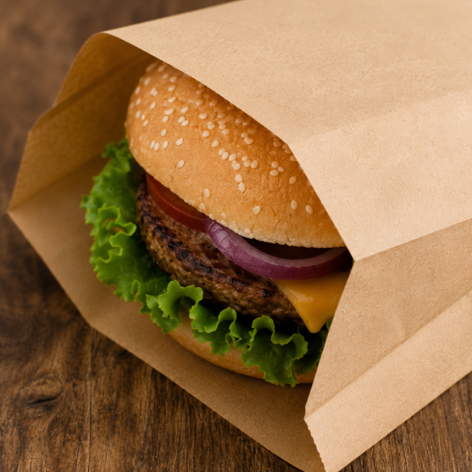 Close-up van een verse hamburger in een bruin FSC papieren hamburgerzakje van kraftpapier. Het zakje biedt een duurzame en praktische verpakking voor hamburgers, broodjes en warme snacks.