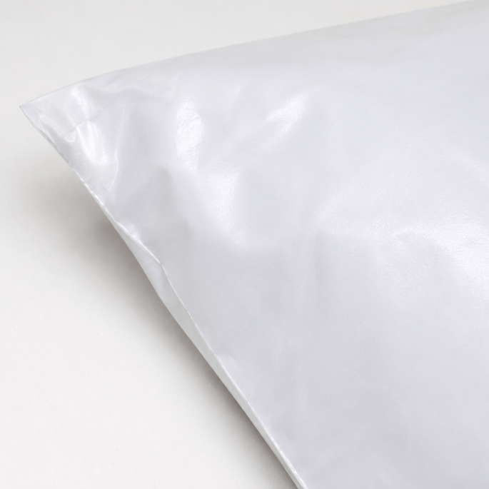 Close-up detailfoto van een witte LDPE verzendzak met glanzende afwerking, waarbij de linkerachterhoek en de textuur van het stevige kunststofmateriaal zichtbaar zijn.