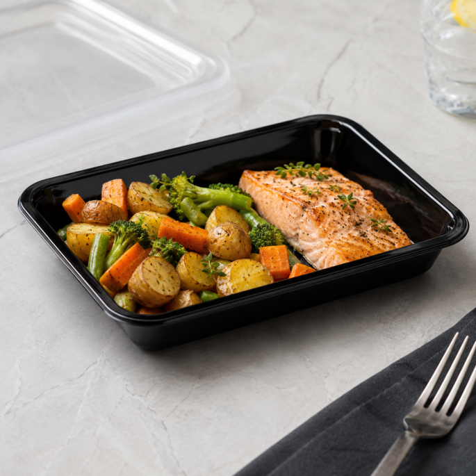 Zwarte PP thermo menuschaal 227 x 178 x 40 mm gevuld met een warme maaltijd van zalm, aardappelen, broccoli, sperziebonen en wortel, gepresenteerd op een licht werkblad als voorbeeld van gebruik voor maaltijdverpakking.